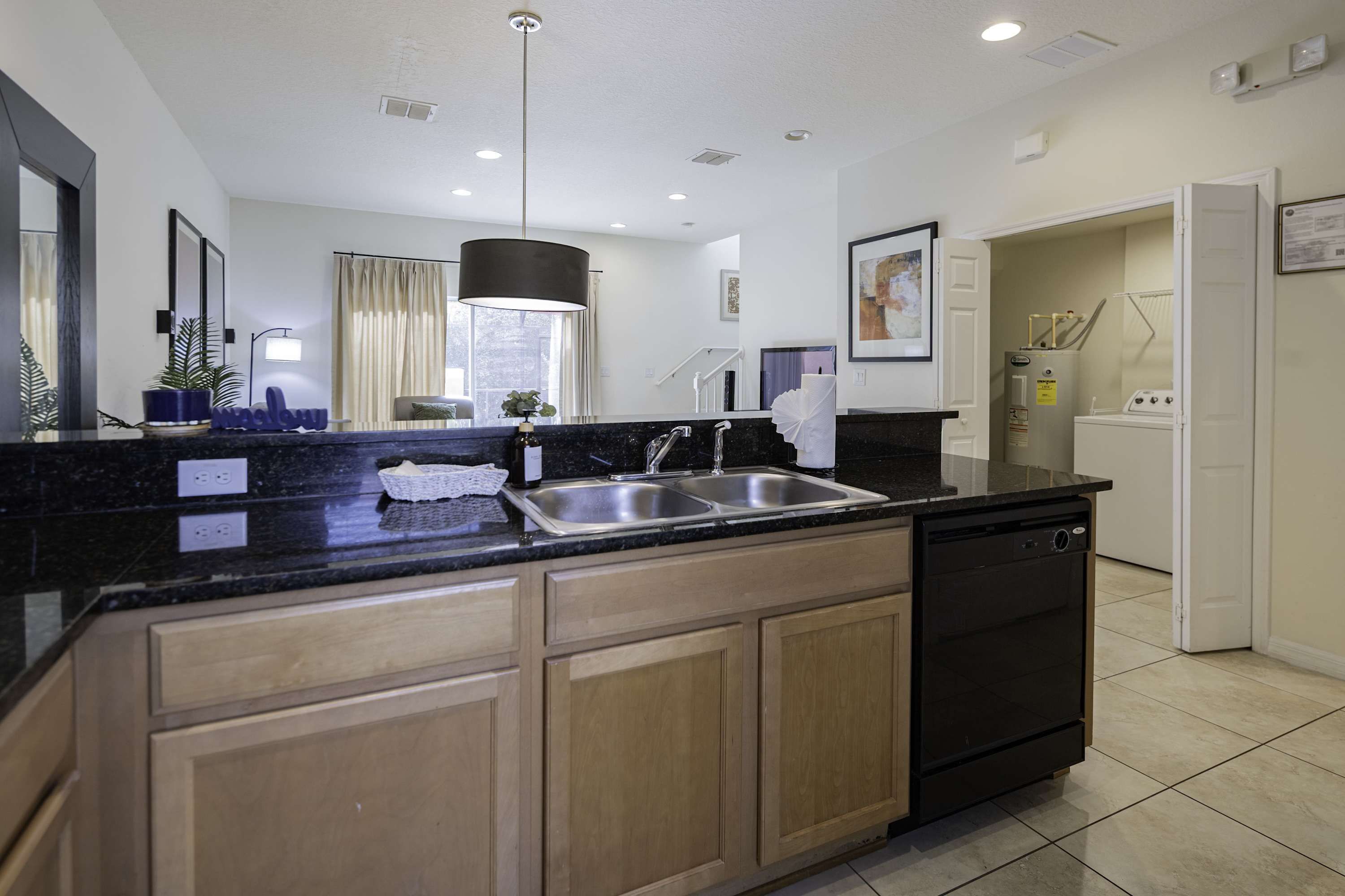 A modern kitchen with a black countertop, stainless steel sink, wooden cabinets, and a built-in dishwasher.