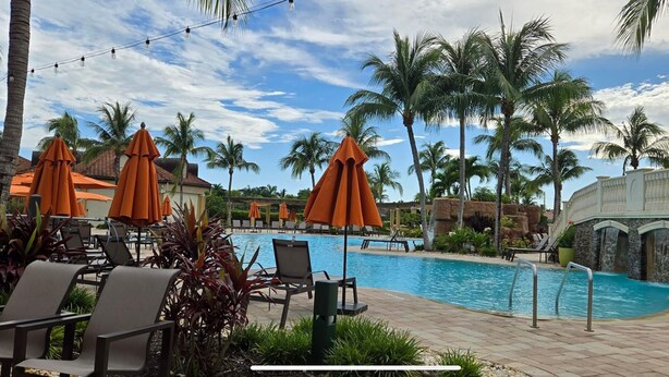 A poolside area with orange umbrellas, lounge chairs, and palm trees.