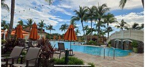 Un espace aménagé au bord de la piscine, avec des parasols orange, des chaises longues et des palmiers.
