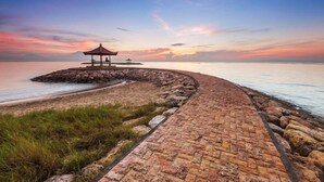 Uma trilha de pedra leva a um gazebo à beira-mar durante o pôr do sol.