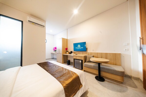 A modern hotel room with a bed, a small desk, a seating area, and a television on the wall. - Sascanaluna Padma Bali (Penatih)
