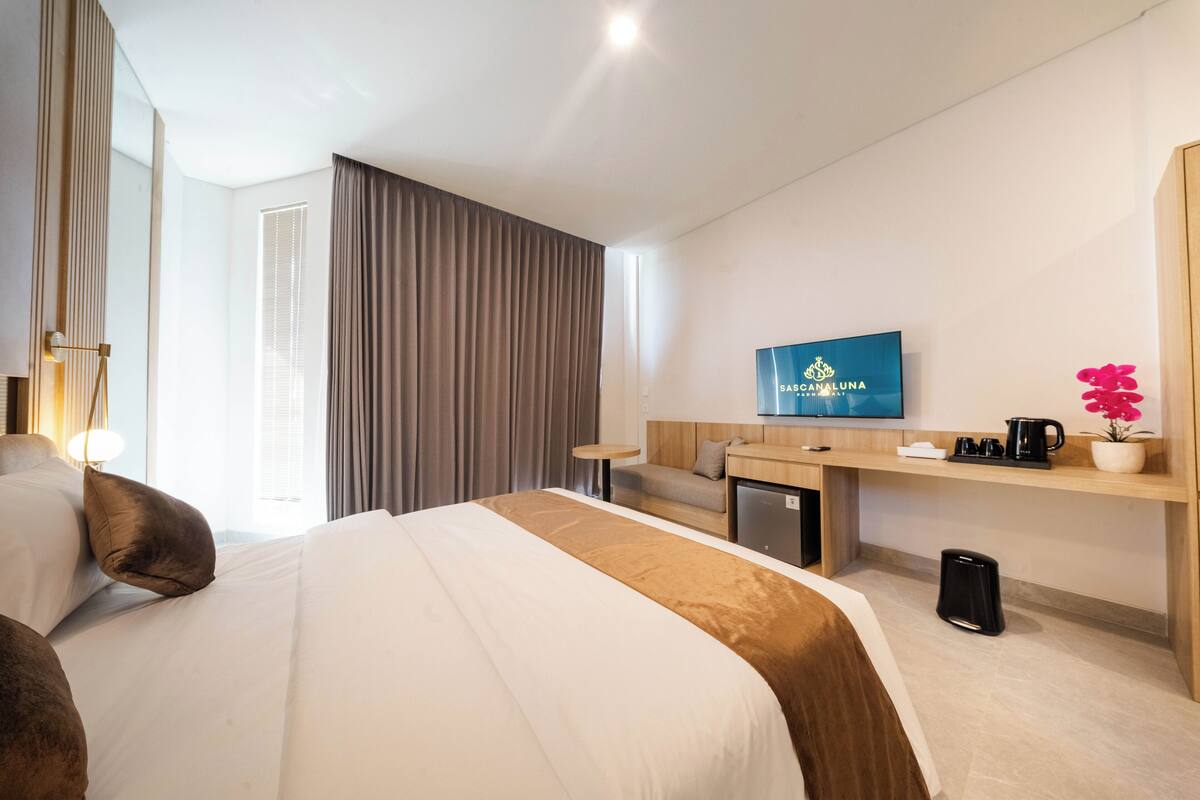 Een hotelkamer met een groot bed, een aan de muur bevestigde televisie, een klein bureau en een koffiezetapparaat.