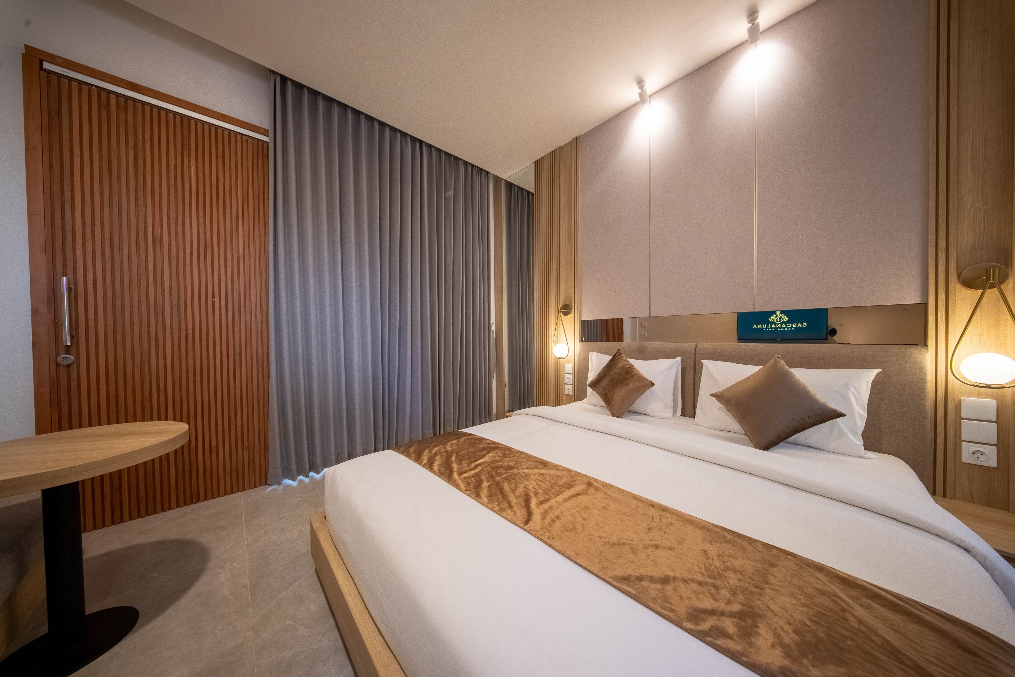 Una camera d'albergo con un letto, una porta in legno, un tavolo e una lampada a parete.