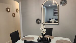 Uma área de refeições com mesa branca, cadeiras pretas, um lustre e arte decorativa na parede.