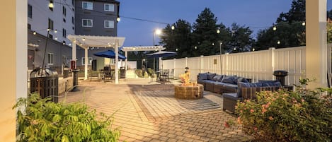 An outdoor patio area with a fire pit, seating, and string lights.