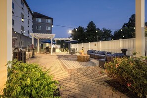 An outdoor patio area with a fire pit, seating, and string lights. - Candlewood Suites Stafford - Quantico by IHG (Stafford)