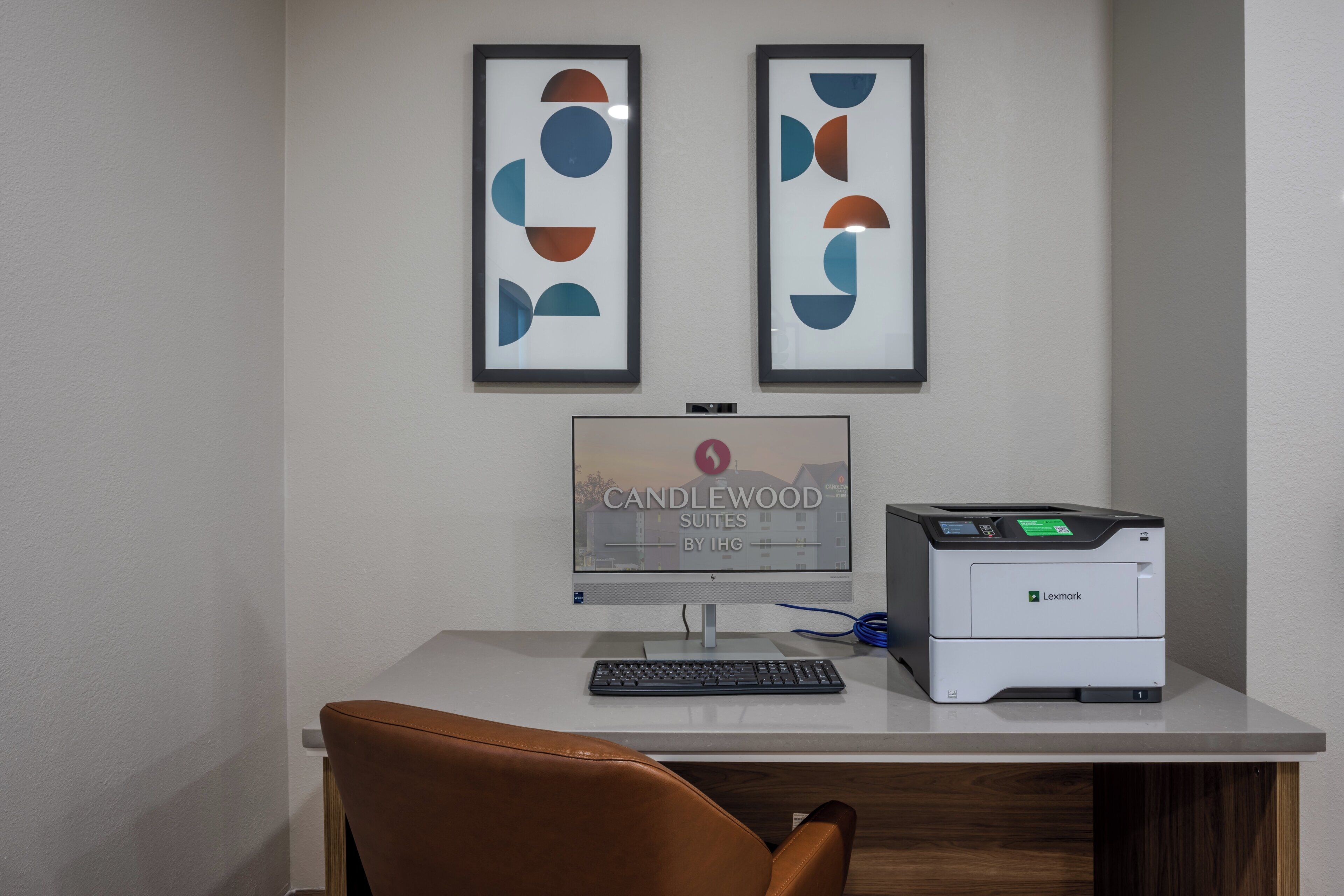 A desk with a computer, a printer, and two framed abstract artworks.