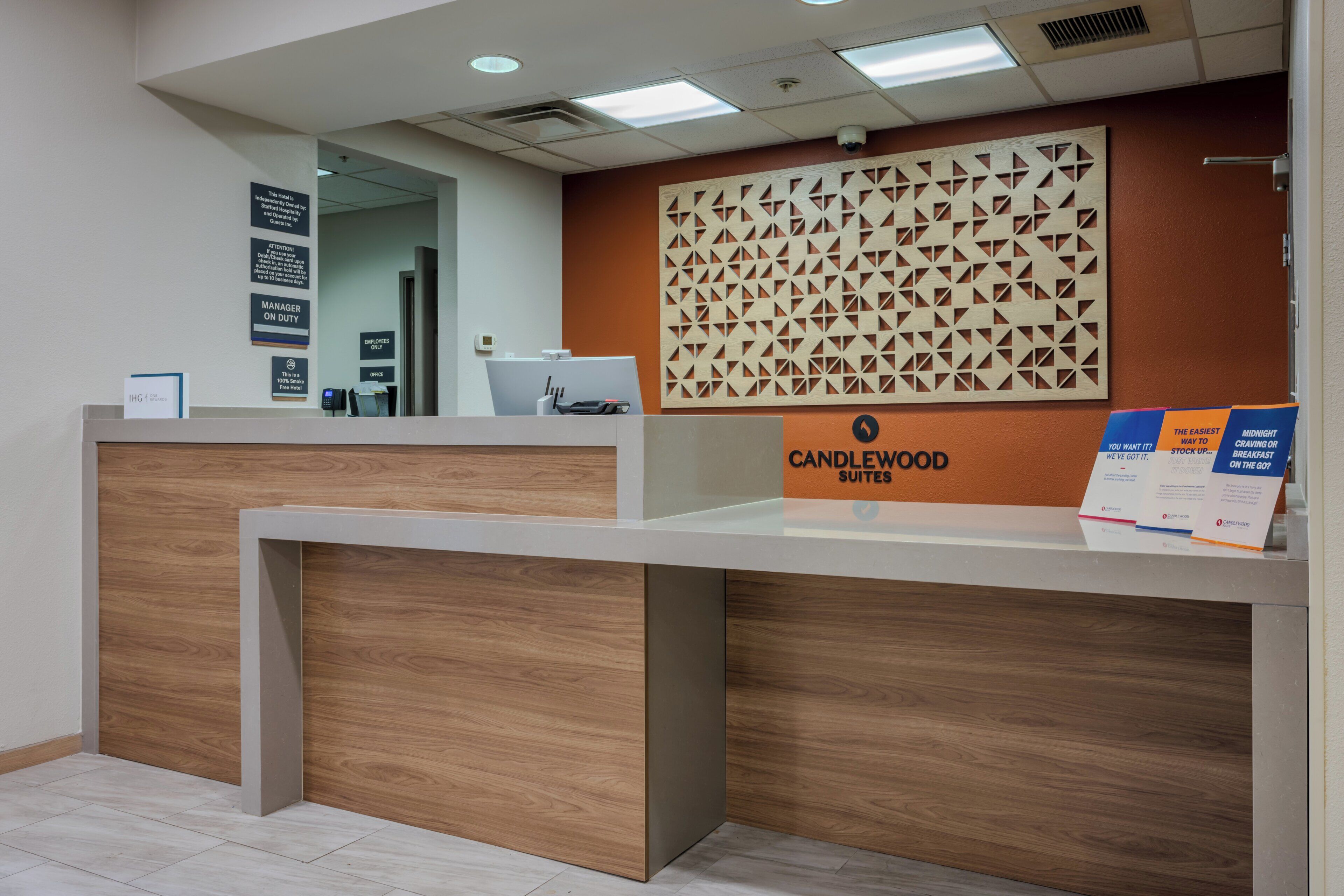 A hotel reception desk with a modern design, a sign for Candlewood Suites, and a security camera above the desk.