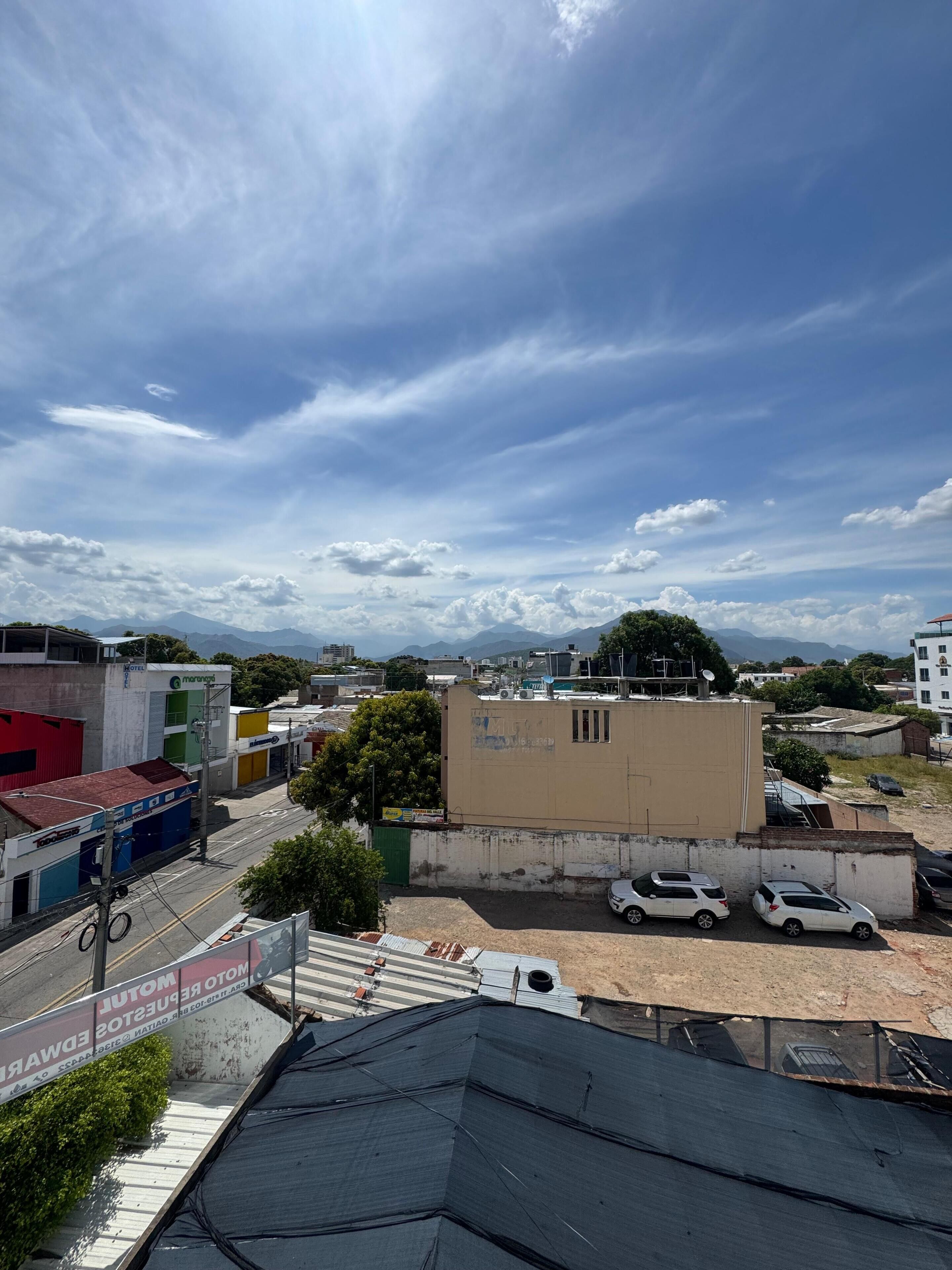 A hotel with a flat roof, a signboard, and a parking area with cars.