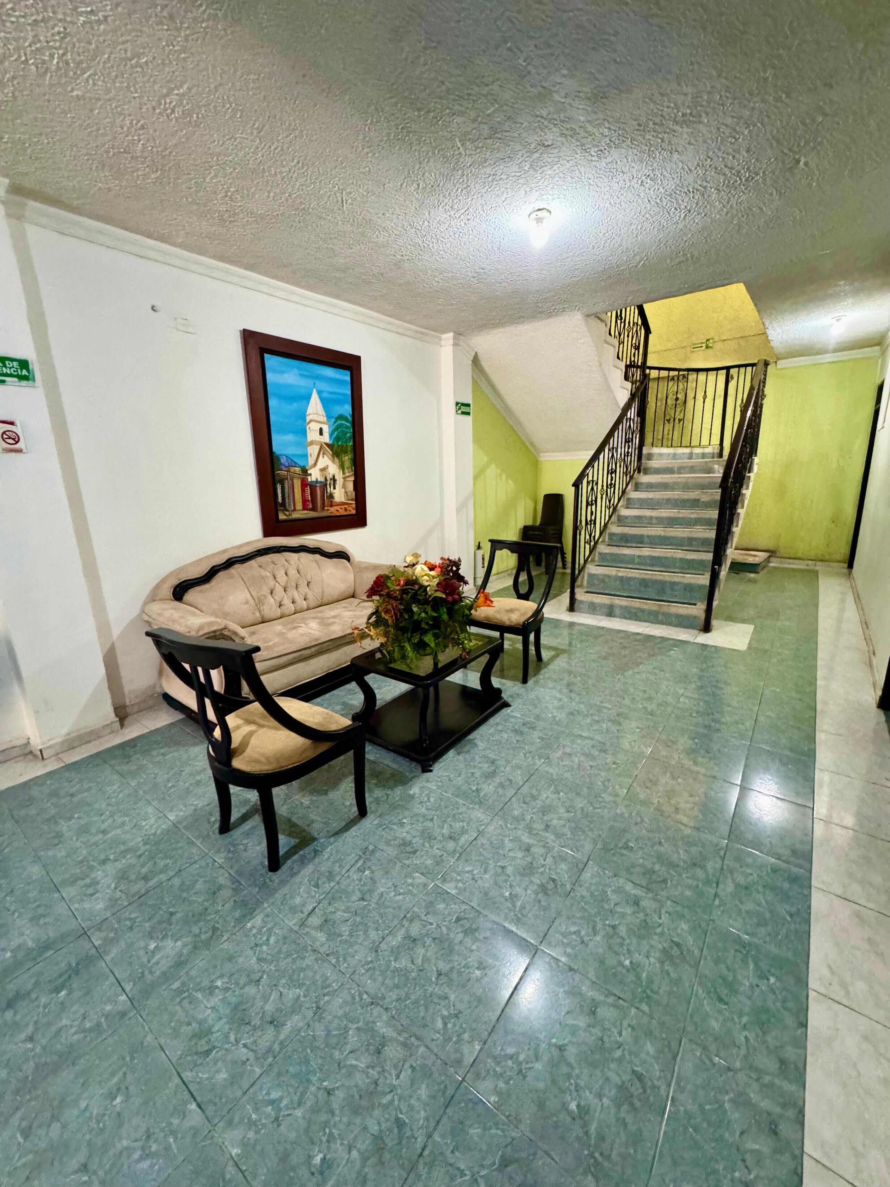 Un vestíbulo con un sofá, sillas, una mesa baja con flores, una escalera y un cuadro en la pared.