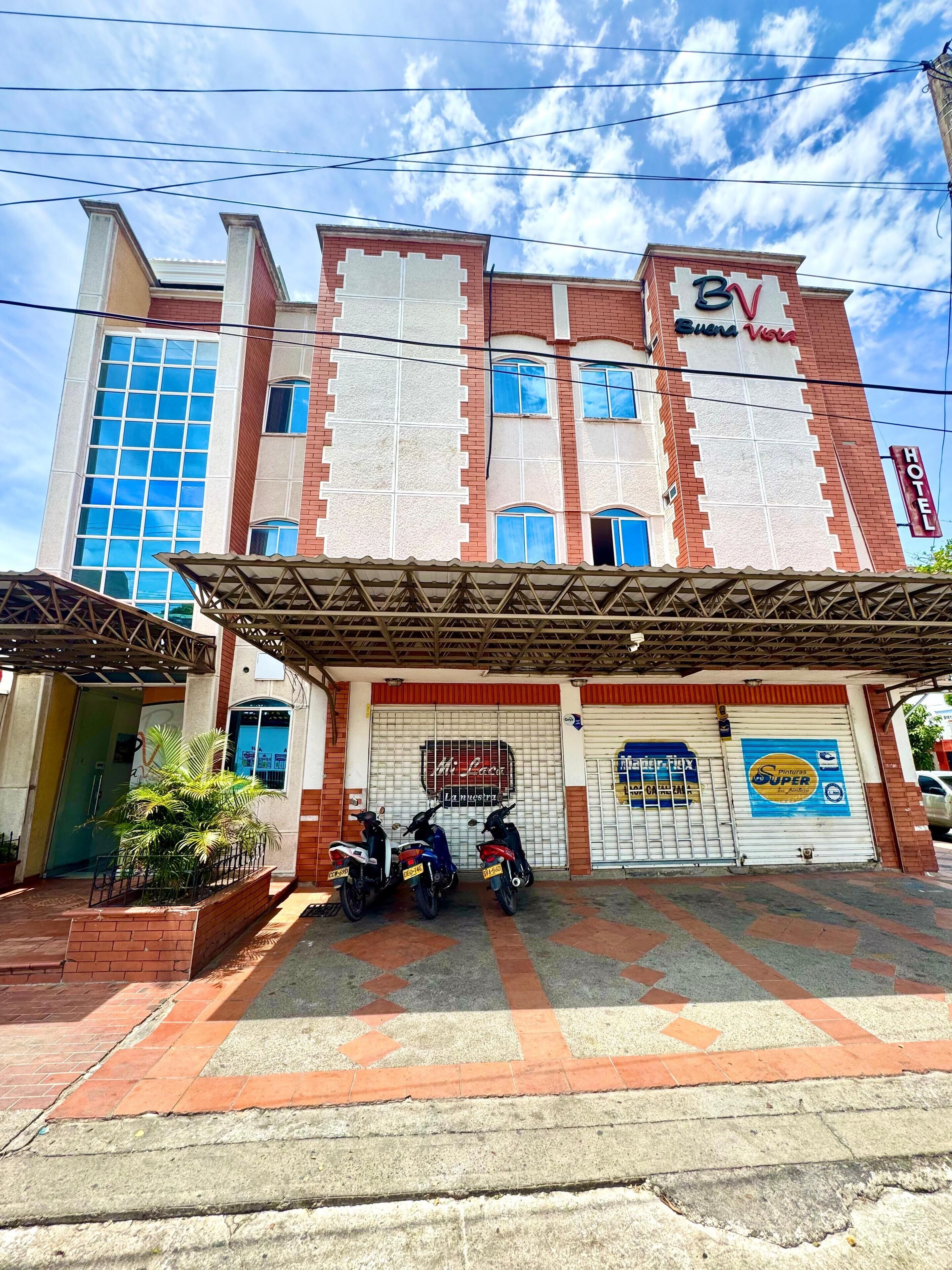 A hotel with a prominent 'BV' sign, a covered entrance, and a tiled pavement.