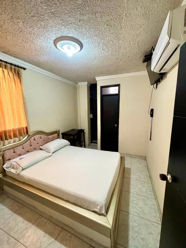 A bedroom with a bed, a desk, a chair, a door, and an air conditioning unit. - Hotel Buenavista Valledupar (Valledupar)
