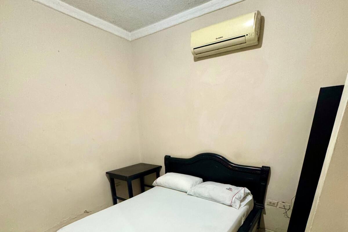 A bedroom with a bed, a small table, and an air conditioning unit on the wall.