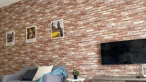 A living room with a brick wall, a grey sofa, a small white table with a plant, and a wooden TV stand. - Cameron Golden Hill Near Night Market CH1 (Brinchang)
