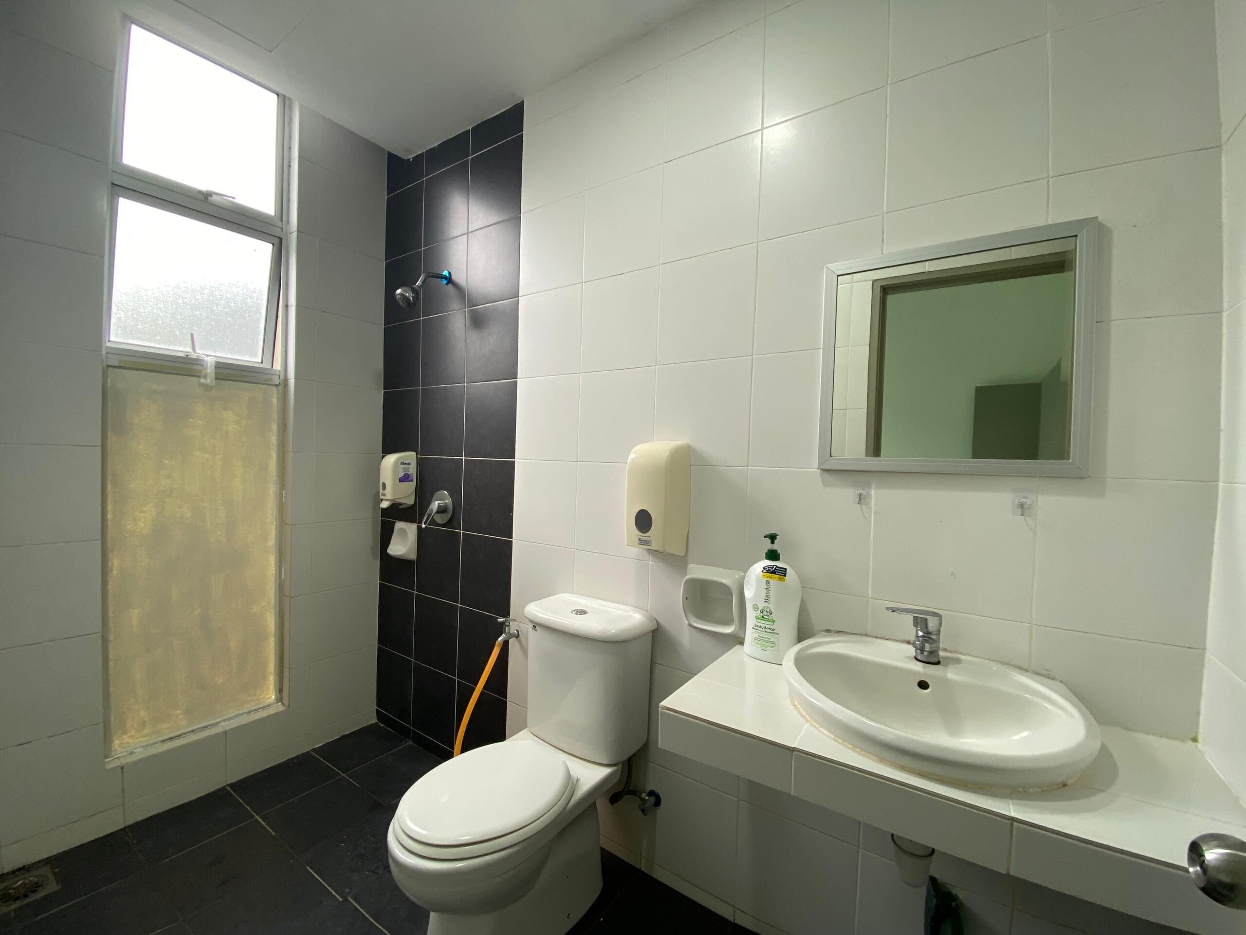 Une salle de bain avec des toilettes, un lavabo, un miroir et une fenêtre.