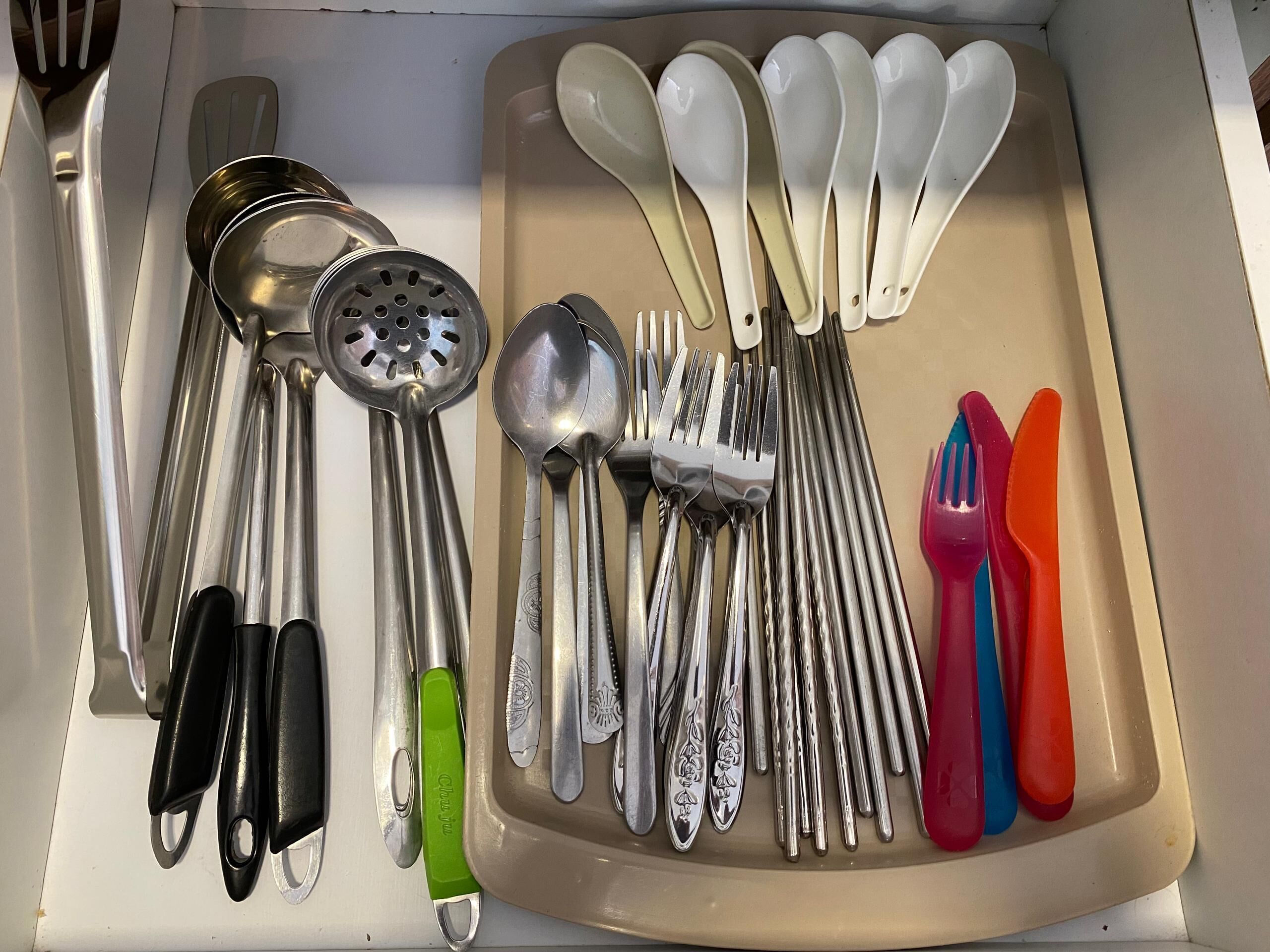 A drawer containing various kitchen utensils including spoons, forks, and a grater.