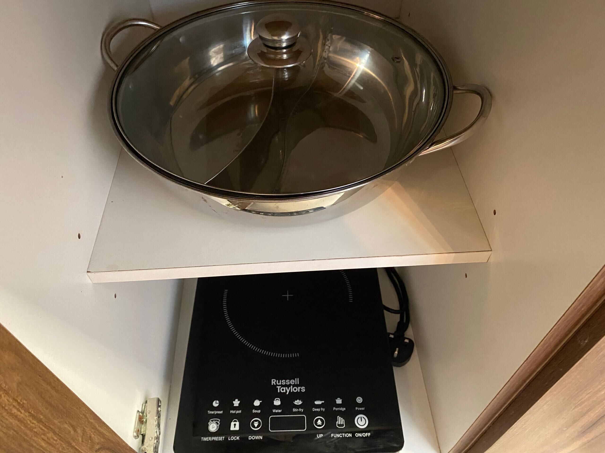 Una cucina con una pentola di vetro su un piano di lavoro bianco e un piano cottura a induzione nero sottostante.