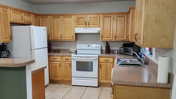 Una cocina con armarios de madera, un refrigerador blanco, una estufa y un cubo de basura.