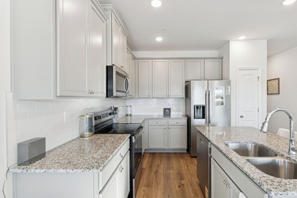 A modern kitchen with white cabinets, granite countertops, stainless steel appliances, and a wooden floor. - The Jonesboro Treasure (Jonesboro)