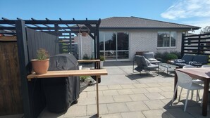 An outdoor patio with a pergola, seating area, and a view of a house.