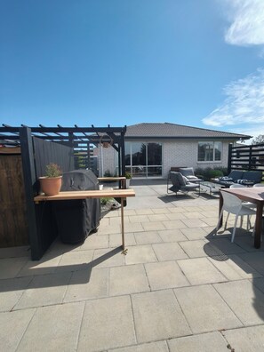 Patio esterno con pergolato, area salotto e vista su una casa.