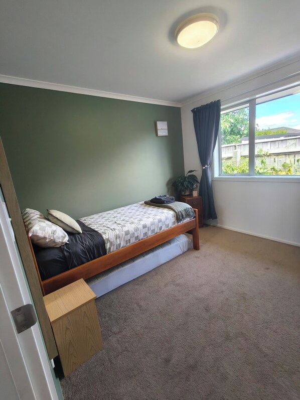 Une chambre avec un lit simple, une petite table de chevet, une fenêtre avec des rideaux et un luminaire au plafond.