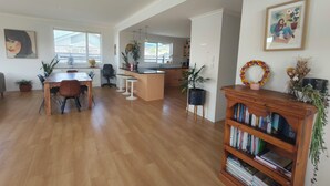 A spacious living area with a wooden dining table, bar stools, a kitchen with a large island, and a bookshelf filled with books.