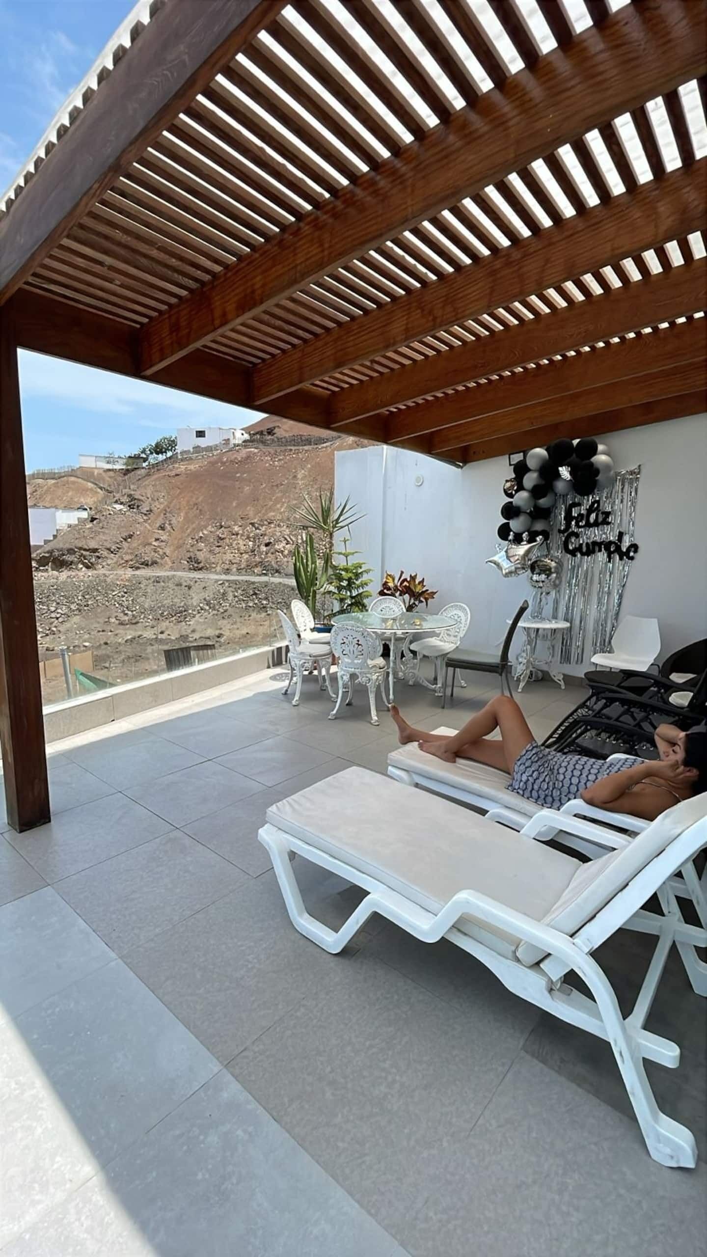 Un espace extérieur aménagé avec une pergola, une table et des chaises, et un mur décoratif orné de ballons.