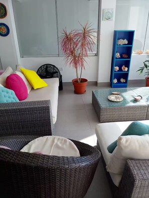 A modern living room with wicker furniture, a potted plant, and a blue shelving unit with decorative items. - Enchanting 3-bedroom apartment in Naplo (Pucusana)