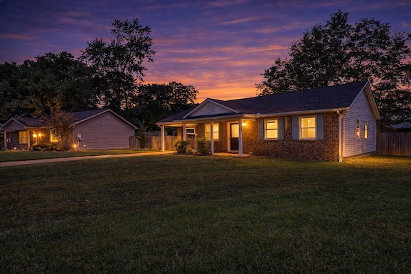 A residential house with a well-maintained lawn, a front porch, and a garage. - 3BR Home Near Southside Complex, Fast WiFi, Fenced Yard, Sleeps 6 (Jonesboro)