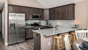 A modern kitchen with dark wood cabinets, stainless steel appliances, a granite countertop, and a bar area with stools.