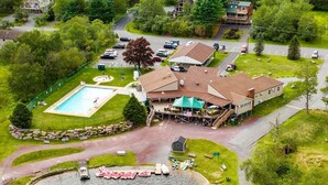An aerial view of a lakeside property with a swimming pool, dock, and a building with a covered patio.
