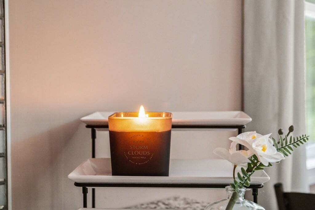 A lit candle on a white shelf with a label reading "STORM CLOUDS."