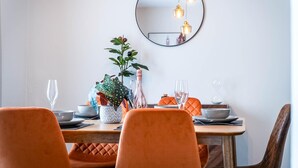 Ein Essbereich mit einem runden Spiegel, orangefarbenen Stühlen und einem Tisch, der mit Tellern, Gläsern und einer Pflanze gedeckt ist.