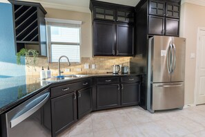 Una cocina moderna con armarios oscuros, un refrigerador de acero inoxidable y una ventana con persianas.