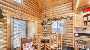A log cabin interior with a wooden dining table, chairs, and a hanging light fixture.