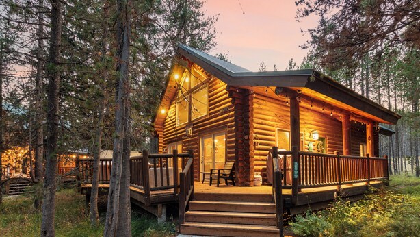 A log cabin with a porch, wooden steps, and a view of the surrounding forest.