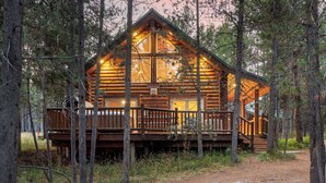 A log cabin with a wooden deck and large windows, surrounded by trees.