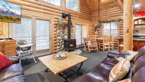 A log cabin interior with a stone fireplace, wooden furniture, and a dining area.