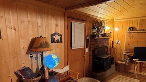 En mysig stuga med träpanel på väggarna, en öppen spis, en tv och en jordglob på ett bord.