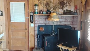 Ett mysigt rum med en trädörr, en öppen spis, en tv på ett stativ och ett litet bord.