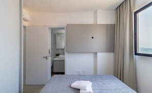 A modern hotel room with a bed, a large window with curtains, a flat-screen TV, and a visible bathroom with a sink and mirror. - New Apartment 150m From Pereque Beach Cle1202 (Porto Belo)