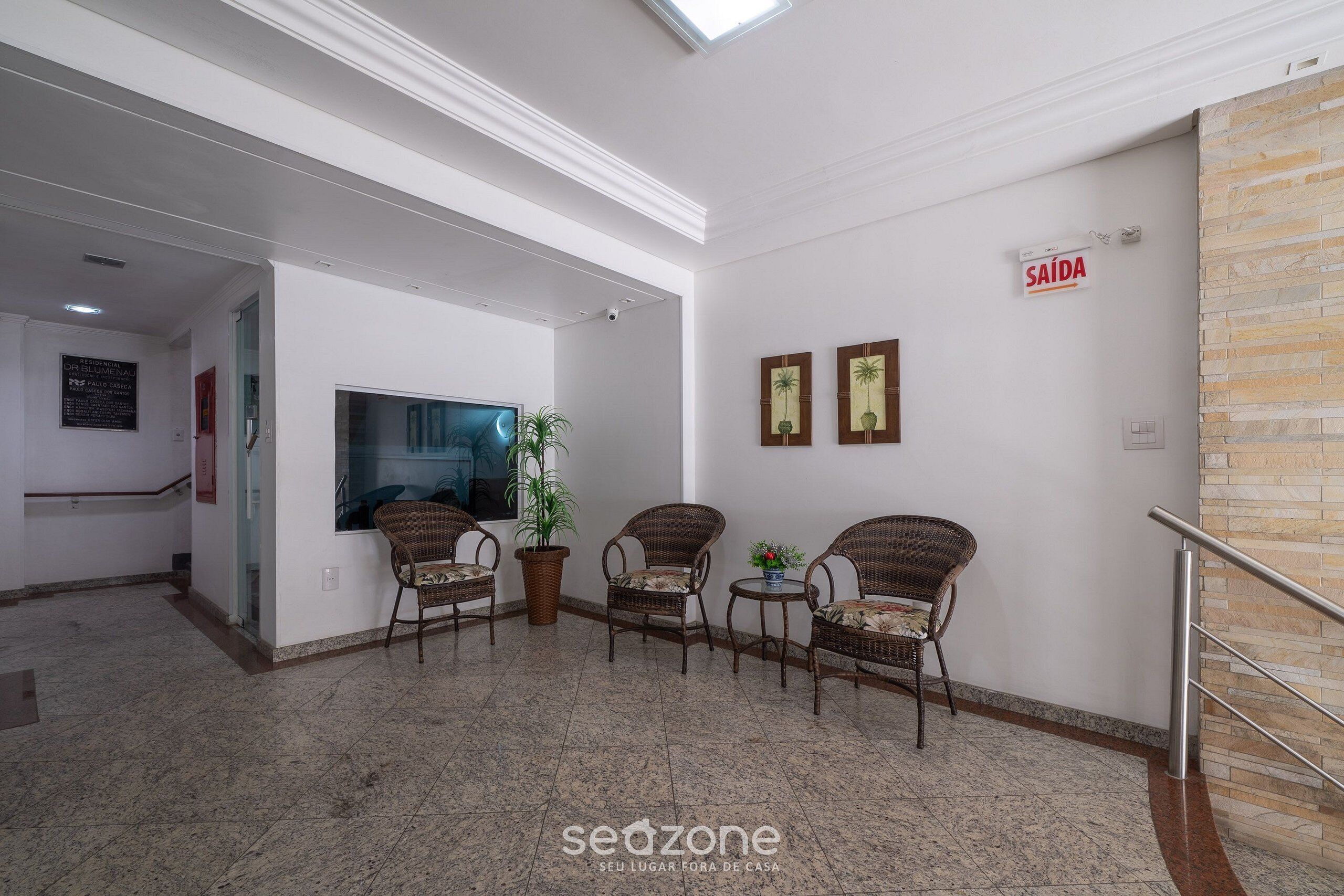 A lobby with a reception desk, wicker chairs, a potted plant, and a sign indicating the exit.