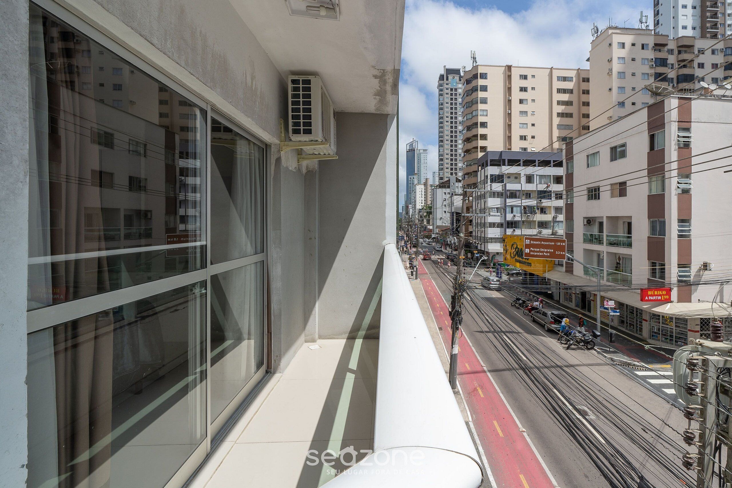 A high-rise building with large windows, a visible air conditioning unit, and a busy street with vehicles and pedestrians below.
