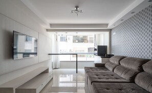 Een moderne woonkamer met een flatscreen televisie, een bank, een eettafel en een behang met patroon.
