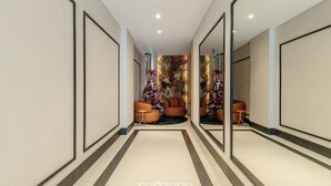 A modern hallway with a central seating area featuring orange chairs and a small table, surrounded by decorative floral arrangements. - Apt Sea View 500m Beach Itapema Dsh1702 (Itapema)