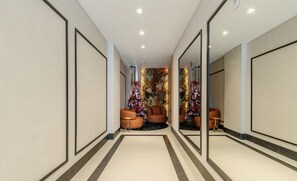 A modern hallway with a central seating area featuring orange chairs and a small table, surrounded by decorative floral arrangements. - Apt Sea View 500m Beach Itapema Dsh1702 (Itapema)