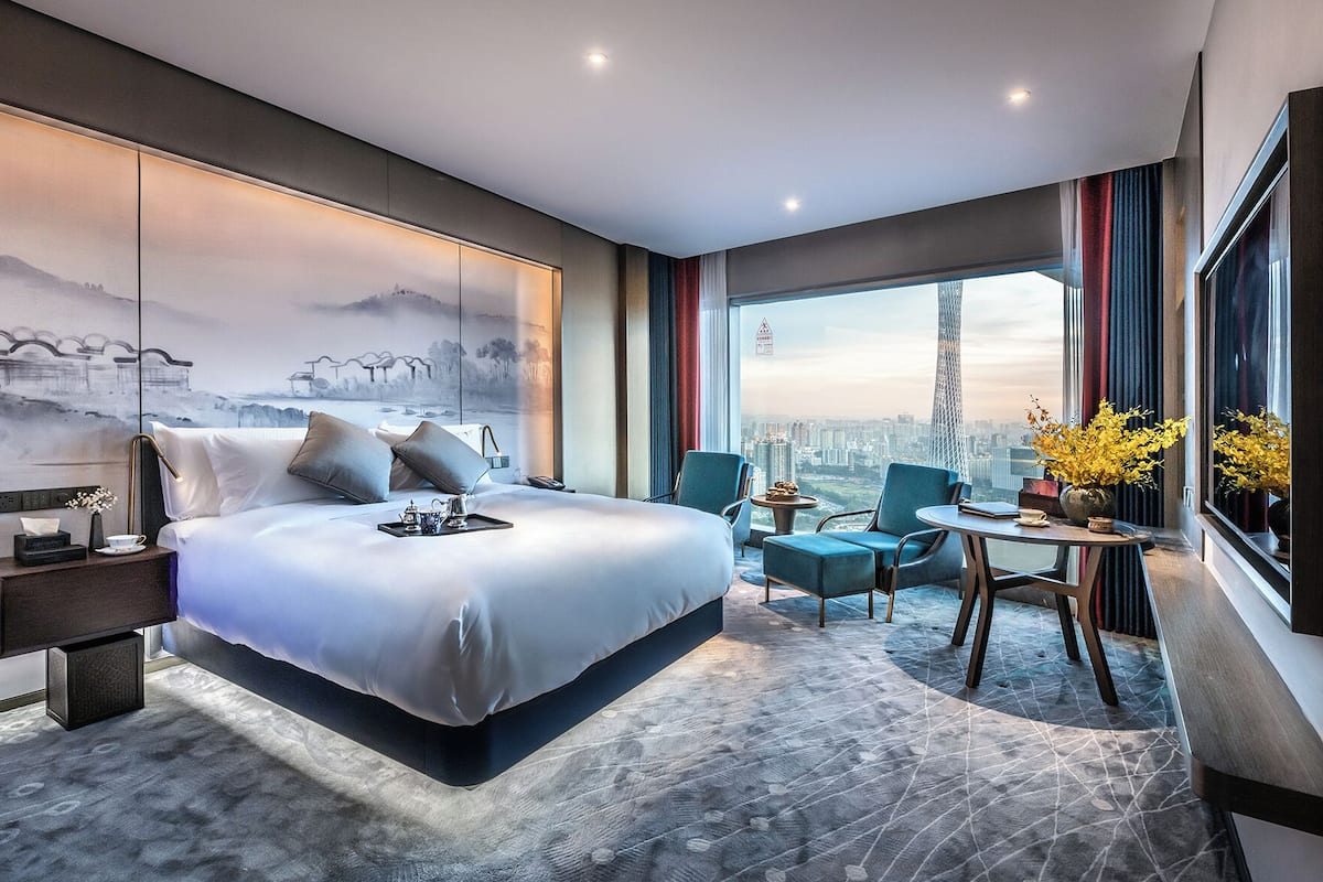Una habitación de hotel moderna con una cama grande, un escritorio y vistas a un paisaje urbano.