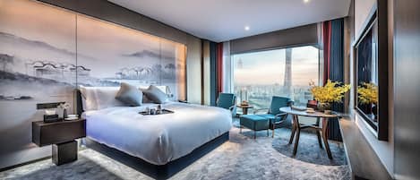 A modern hotel room with a large bed, a desk, and a view of a cityscape.