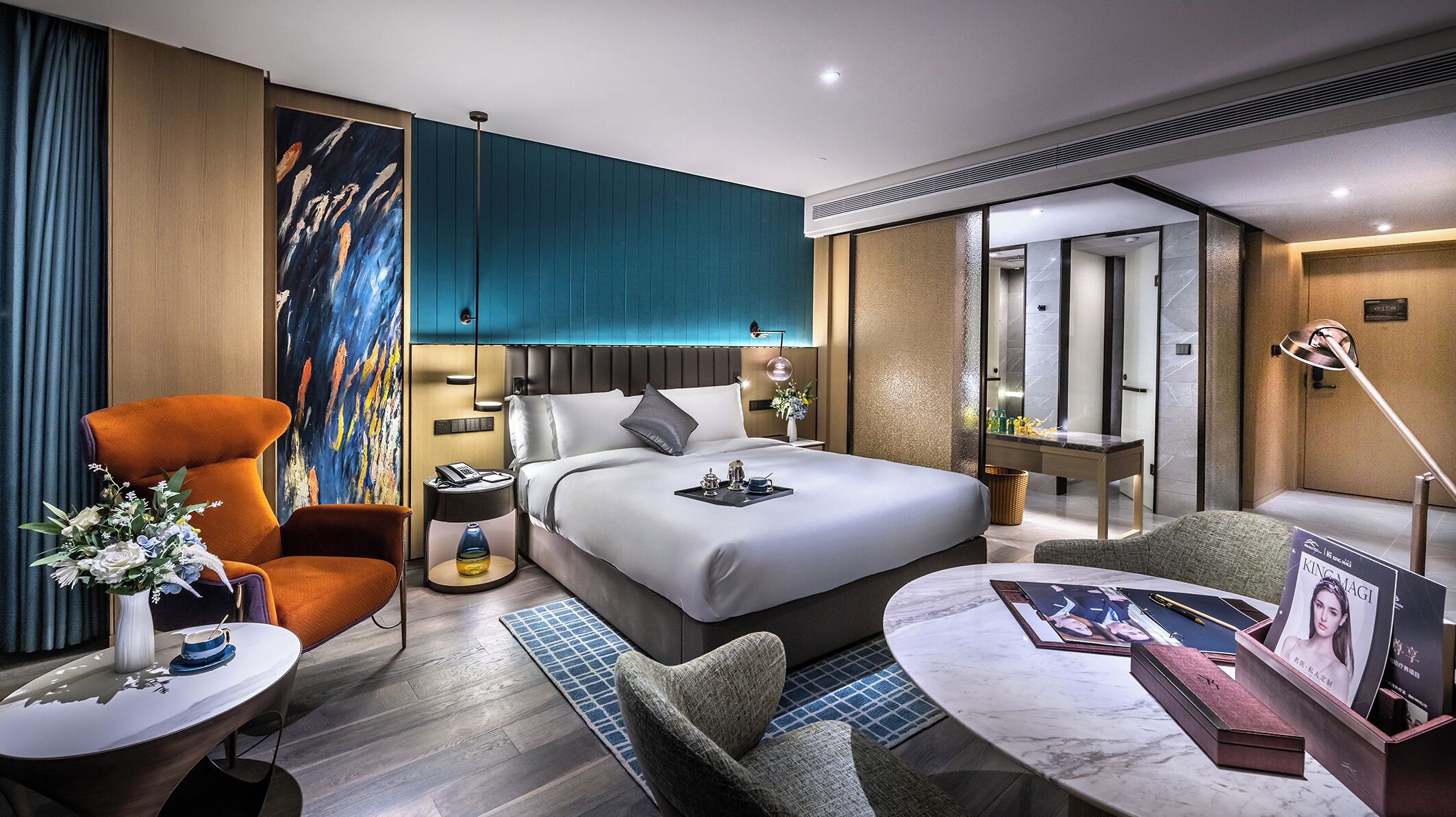 Moderni hotellihuone, jossa on suuri sänky, oleskelualue pöydällä ja tuoleilla, työpöytä tietokoneella sekä suuri ikkuna.